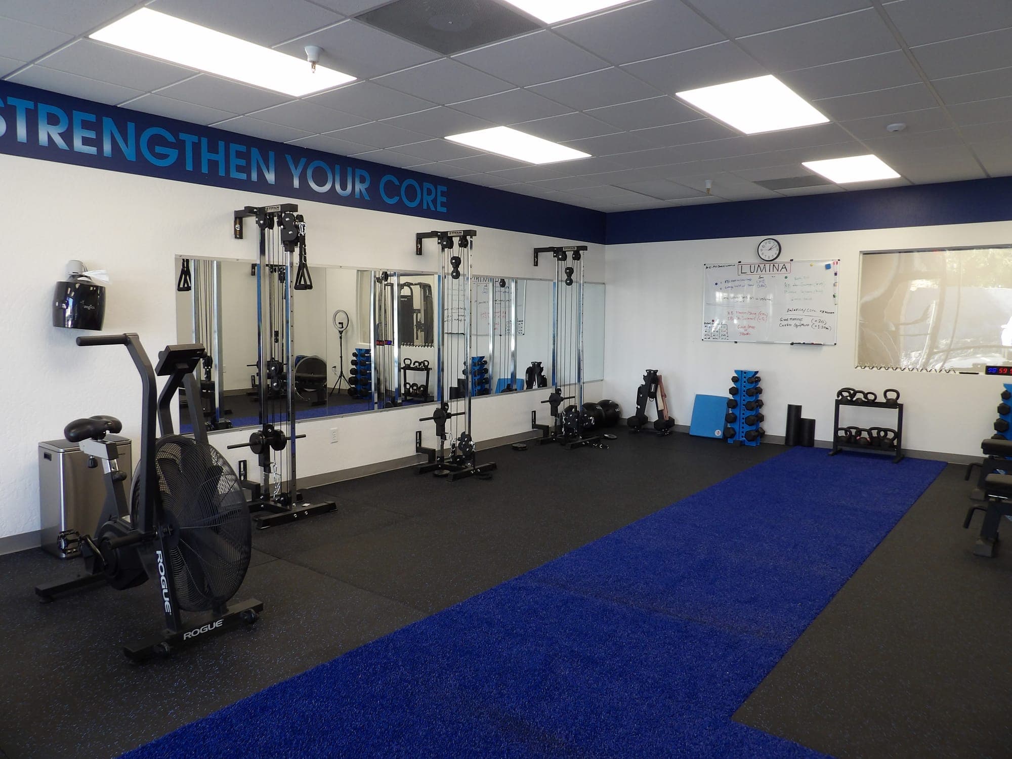 LUMINA exercise studio with an air bike, mirrored wall of cable machines and the class whiteboard