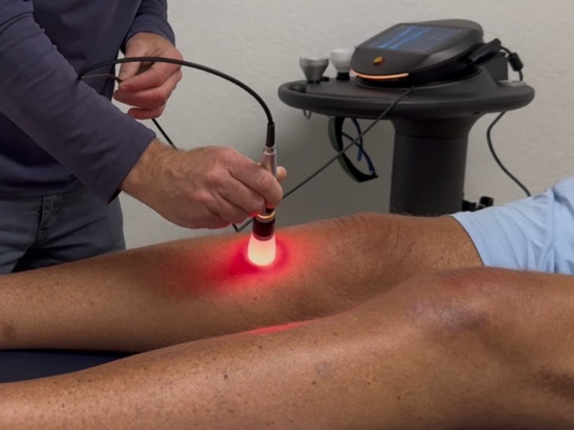 A LUMINA specialist treating a client's knee with the Summus Class IV laser handpiece, the laser unit on its stand behind