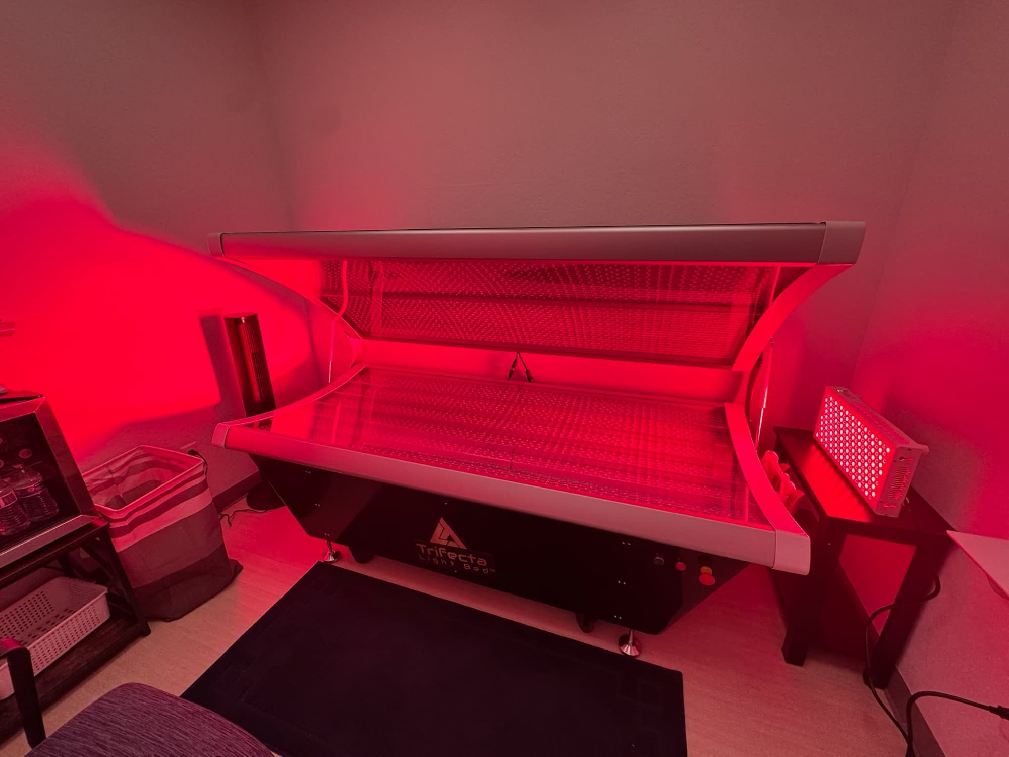 The Trifecta Light full-body red light therapy bed at LUMINA, lid open and glowing red in a private treatment room